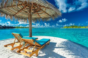 Two beach chairs under umbrella with ocean view in Maldives