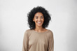 Leinwandbild Motiv Waist up portrait of cheerful young mixed race female with curly hair posing in studio with happy smile. Dark-skinned woman dressed casually smiling joyfully, showing her white straight teeth