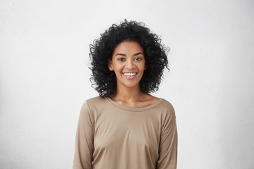 waist up portrait of cheerful young mixed race female with curly hair posing in studio with happy sm