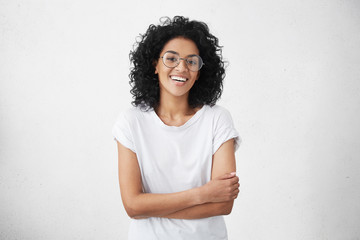 charming young dark-skinned woman with curly hairstyle having shy smile posing in studio in closed p