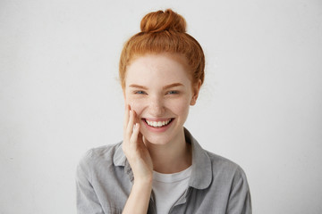 Wall Mural - Youth and happiness. Close up view of beautiful Caucasian teenage woman with long ginger hair and freckles, dressed casually, standing against blank gray wall. Horizontal, isolated, studio shot, model