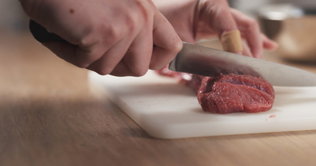 Wall Mural - young female hand cutting raw beef with a knife on plastic board, 4k photo