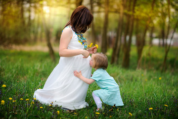 pregnant mother walks in the park with the daughter on a sunset, the girl kisses mother's tummy gently