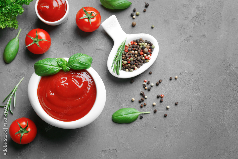 Delicious ketchup in bowl with ingredients on dark background, top view
