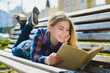 © dreamsnavigator - Little pretty girl reading a book and sitting on bench outdoor