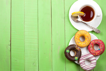 Wall Mural - glazed donuts with a cup of tea on a green wooden background with copy space for your text. Top view