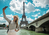 Fototapeta Paryż - Woman tourist selfie near the Eiffel tower in Paris under sunlig