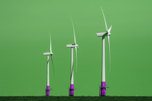 Green Energy Production. Group Of Three Wind Turbines In Profile Against Colour Manipulated Background Representing The Rise Of Green Renewable Energy Production.