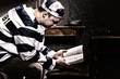 © kolotype - Male prisoner wearing prison uniform reading a book or a bible while sitting on a bed in a prison cell