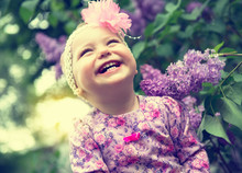 Beautiful Little Girl Playing In Spring Park, Lilac Flowers Garden. Childhood. Cute Kid's Face Over Nature Background. Cheerful Child's Portrait, Soft Focus.