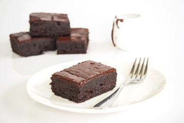 Sliced brownies on white plate. Served with chocolate fudge. On white plate over white background. Sweet and moist chocolate dessert.