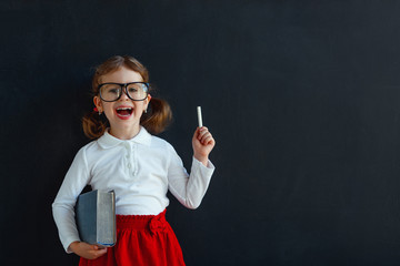 Wall Mural - Happy schoolgirl preschool girl with book near school blackboard