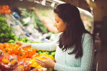 Closeup portrait, young woman in green sweater picking bell peppers with lots of options at grocery store, isolated produce background