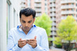 © ashtproductions - Closeup portrait of guy in blue shirt seeing stunning text messages on cell smart phone, isolated city outside background