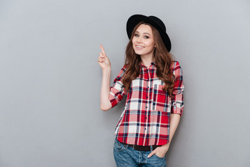 Wall Mural - Cheerful girl in plaid shirt pointing finger up at copyspace