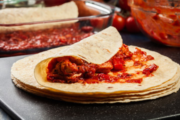 Preparation traditional mexican enchiladas with chicken meat, spicy tomato sauce and cheese