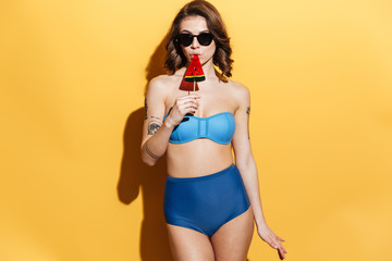 Wall Mural - Serious young lady in swimwear isolated over yellow background