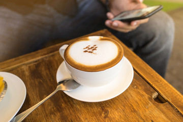 hot coffee on wooden table with man using his phone in background