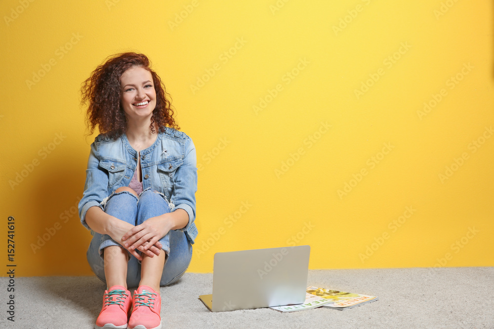 Beautiful young woman with laptop on color wall background