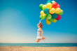 © Sunny studio - Happy child jumping with colorful balloons on sandy beach