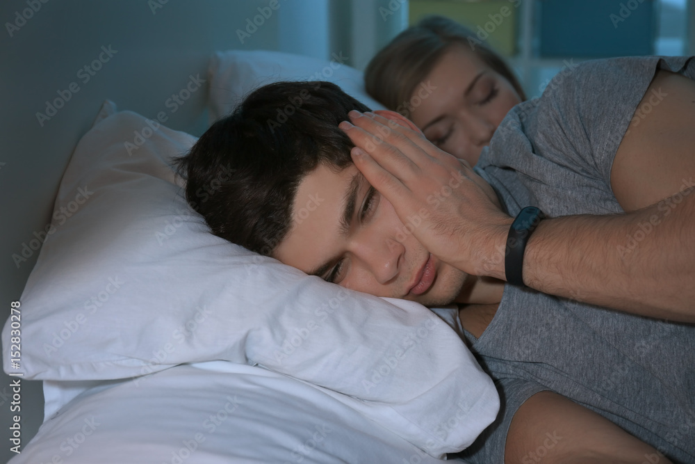 Young man with sleep disorder lying on bed at home