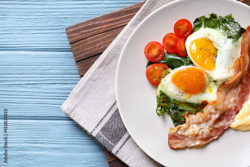 Plate with tasty eggs, spinach and bacon on wooden table