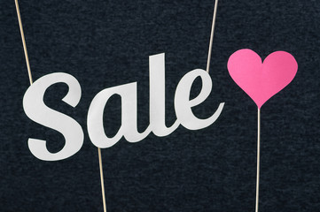 Sale text cut from cardboard paper on wooden stick and dark background. Marketing material for valentine's, women's or mother's day special offer or campaign prices. Nice and fun banner for website.