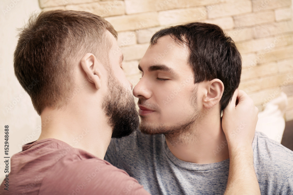 Tender kissing gay couple at home