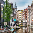 Amsterdam city view canal Singel with colorful dutch house, bridge, the Netherlands with Amstel river, Oudezijds Achterburgwal, reflection Basilica of St. Nicholas Church under dramatic sky in Summer