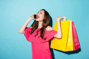 Sticker - Happy young brunette woman holding shopping bags talking by phone.