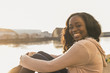 © Westend61 - Young woman sitting at the river, looking at camera