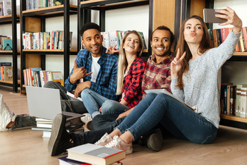 Poster - Happy students sitting in library make selfie by mobile phone.