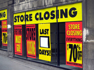 Large printed signs in a department store window announcing store closing and price reductions.