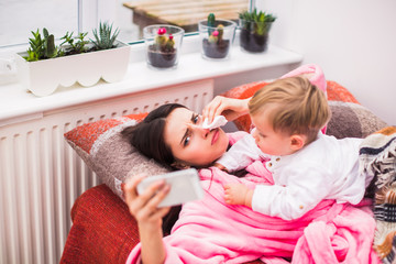 sick young mother lies on bed at home with little son near her and wipes nose of napkin and keeps th