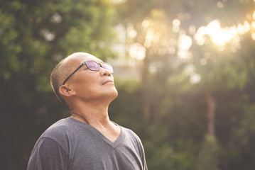 Happiness Asian senior man relaxing and breathing fresh air at park with sunlight.