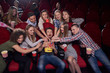 © serhiibobyk - Positive and emotional group of young women and men angry and wanting eating, pulling hands to popcorn to one of boy in center, who screaming. Man holding big bucket with tasty popcorn at cinema.