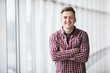 © dianagrytsku - Portrait of smiling man standing with hands crossed in modern building
