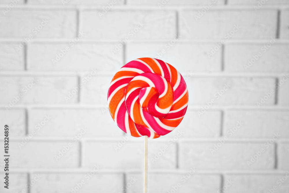 Female hand with tasty lollipop near brick wall
