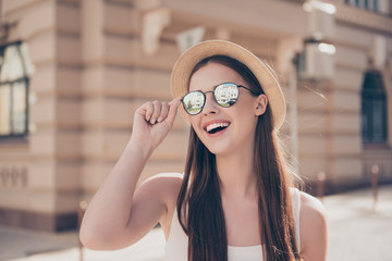 Happy young girl on vacation. She is in a stylish hat and sunglasses, wearing casual singlet, holding her spectacles, amazed