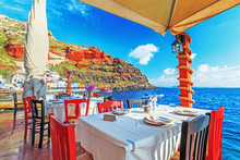 Restaurant At Sea Shore Against Blue Water Of Aegean Sea On Santorini Island Resort In Greece, Europe.