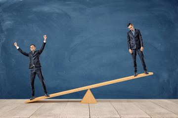 two businessmen standing on a wooden seesaw, one happy and one sad looking.