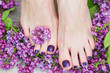 Woman feet with dark purple pedicure and beautiful fresh lilac flowers, beauty treatment