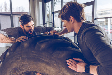 Wall Mural - side view of men pulling tire together while exercising at the gym