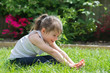 © Liliya Trott - Little girl sitting on the grass in the park doing yoga, reaching her toes, selective focus