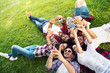 © Tijana - Group of young people laying on the grass in circle, using phones