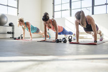 Female Athletes Doing Push-ups On Exercise Mats In Health Club