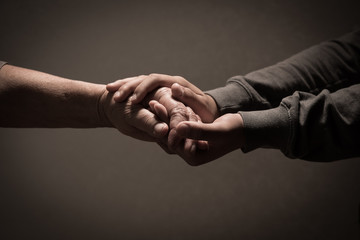 Child hands holding senior woman's hands on brown background