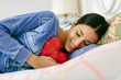 © Emma - Smiling young woman with heart shaped pillow lying on bed