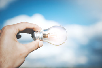 Canvas Print - hand business man holding light bulb on pastel vibrant sky