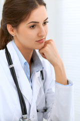 Poster - Latin american female doctor sitting at the table and working by computer at hospital office. The physician or therapist makes a diagnosis. Health care, medicine and patient service concept